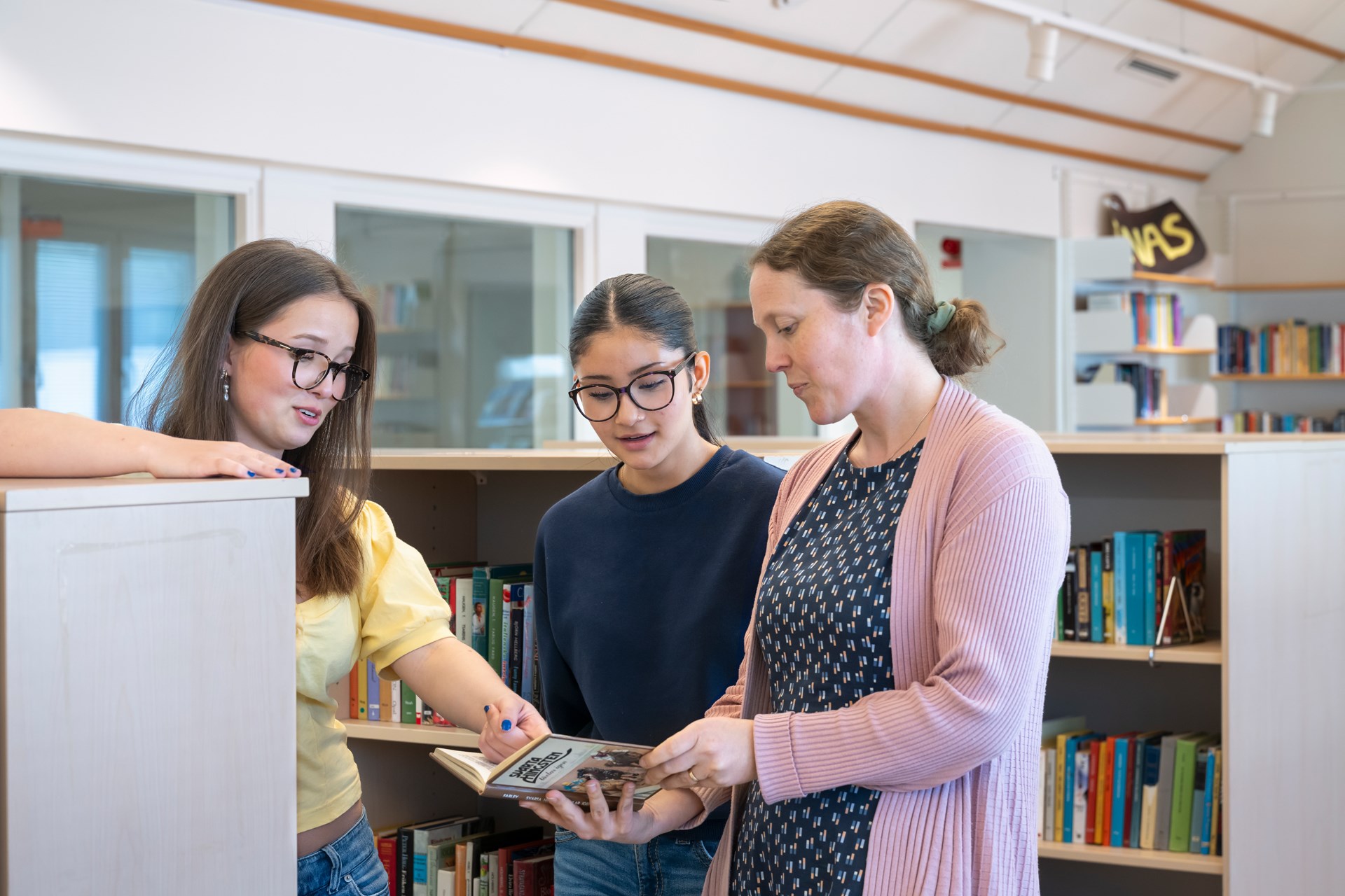Två elever och en lärare i ett skolbibliotek