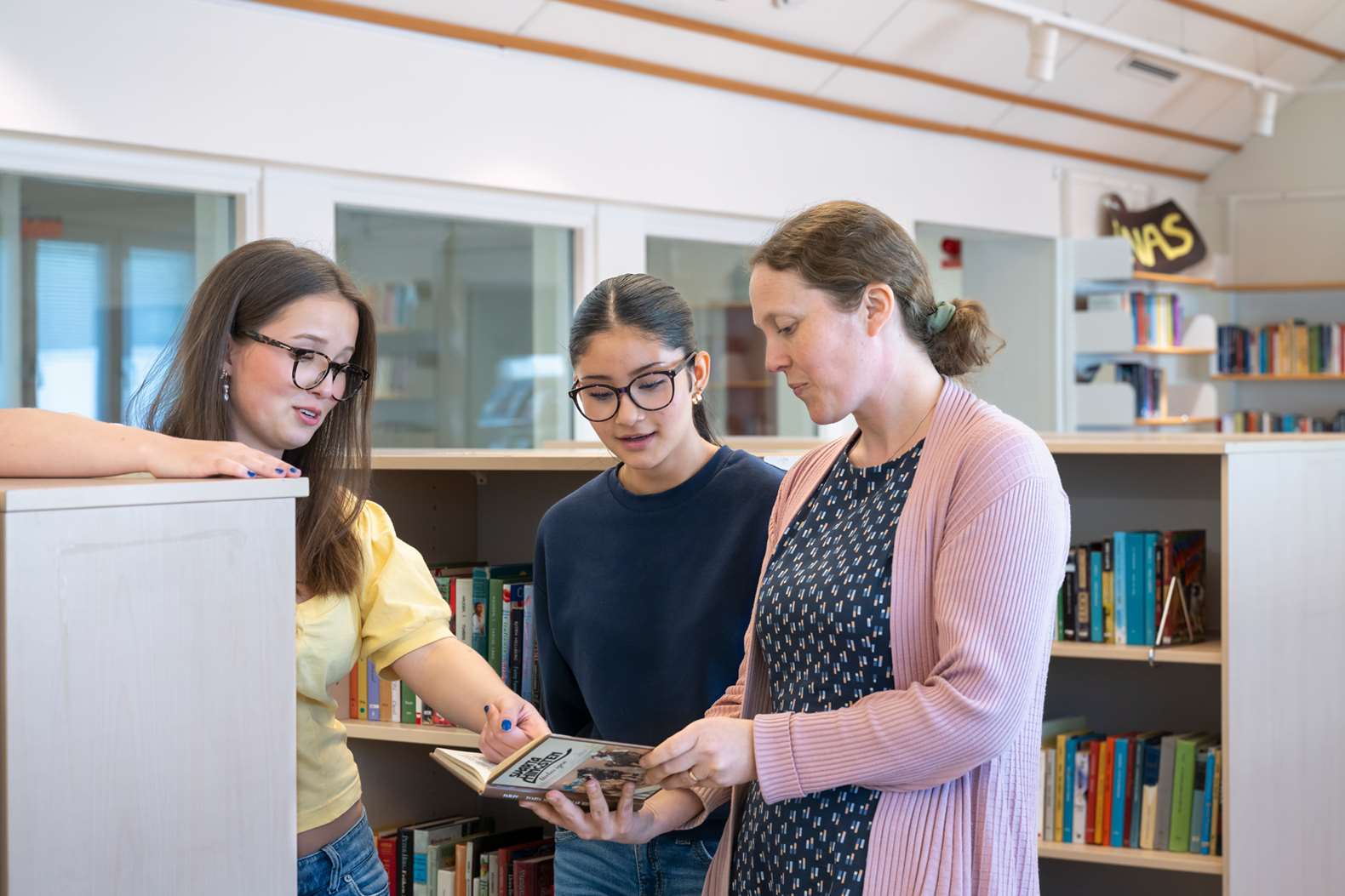 Två elever och en lärare i ett skolbibliotek