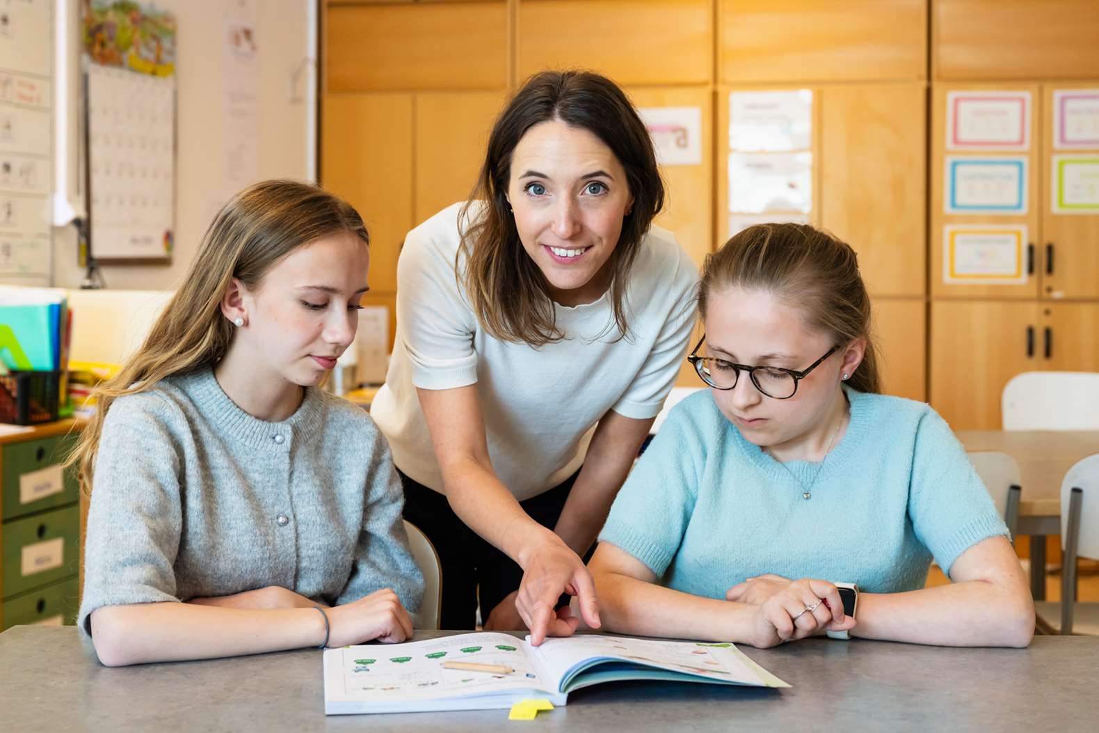 Lärare hjälper två elever och pekar i en bok