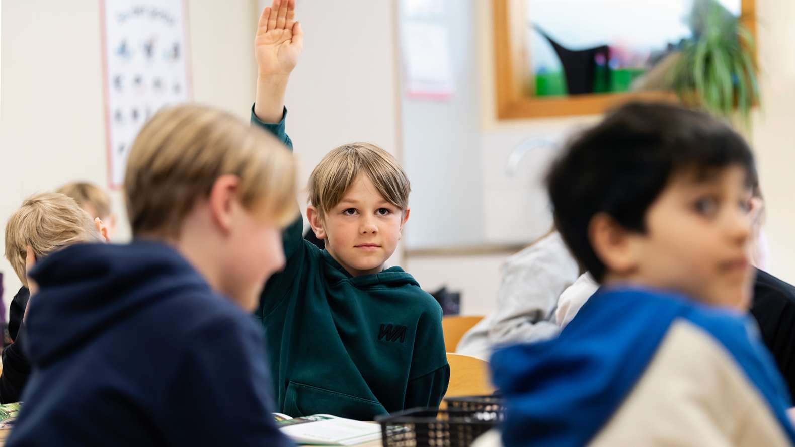 Pojke räcker upp handen i klassrum