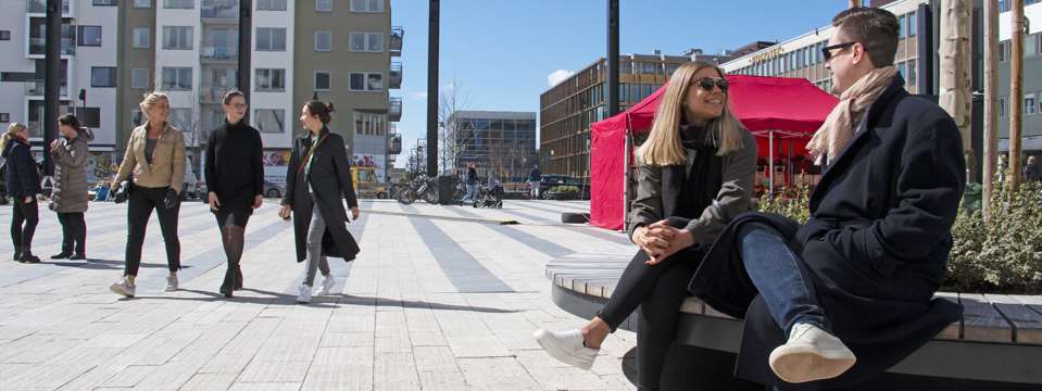 Två personer sitter och fem står och går på Täby torg